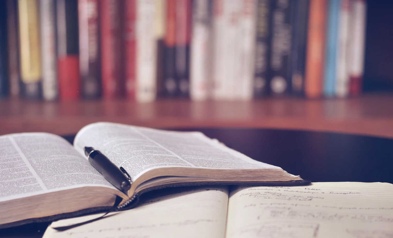 Open book and notebook with a pen on a desk